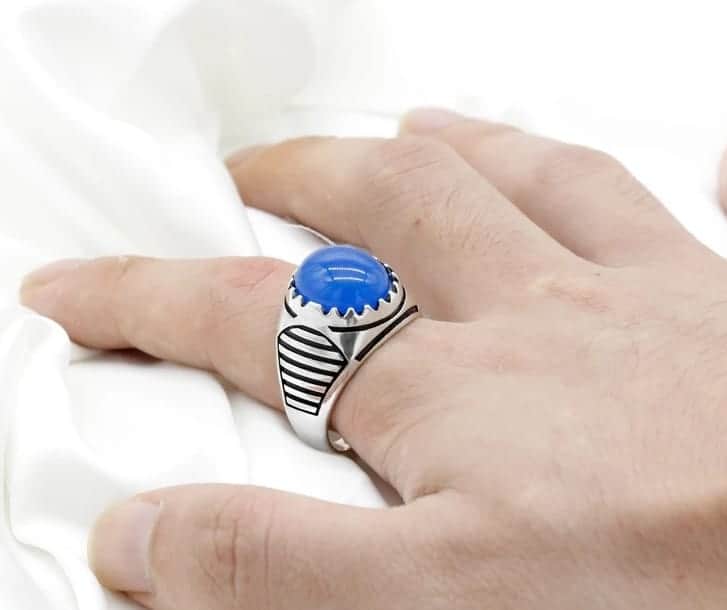 Mann hat einen blauen ovalen Stein-Silberring auf seinem Zeigefinger