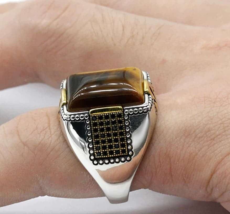 Der Mann hat einen Silber Ring mit einem quadratischen Stein am Zeigefinger.