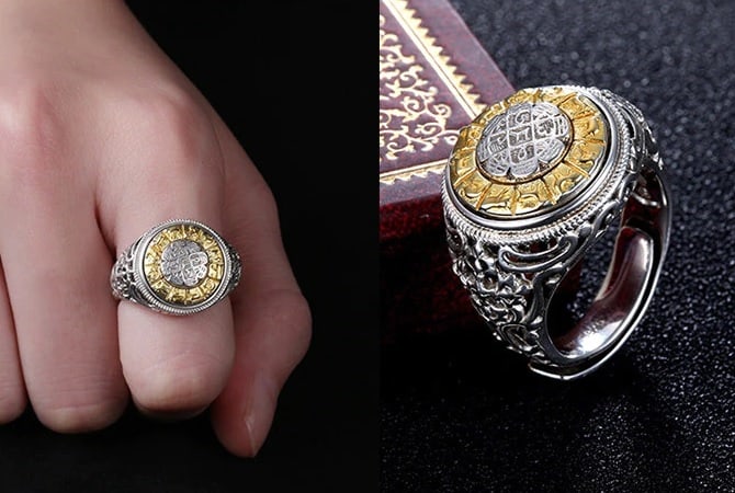 Es gibt zwei quadratische Silber eingelegte Ringe. Auf dem ersten Bild mit dem Zeigefinger auf schwarzem Hintergrund fixiert, dem anderen Bild aufrecht neben dem Buch stehend