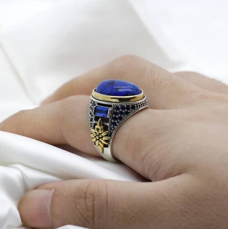 Der Mann hat einen silbernen Ring mit einem großen blauen Stein am Zeigefinger