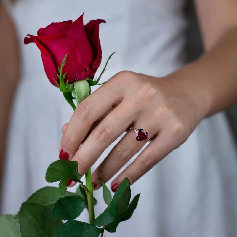 Rote Rose in der Hand der Frau, Ring mit rotem Herzen am Finger