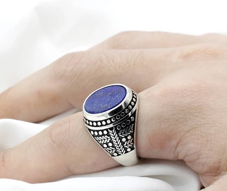 Am Zeigefinger wird ein silberner Ring mit einem blauen Stein getragen
